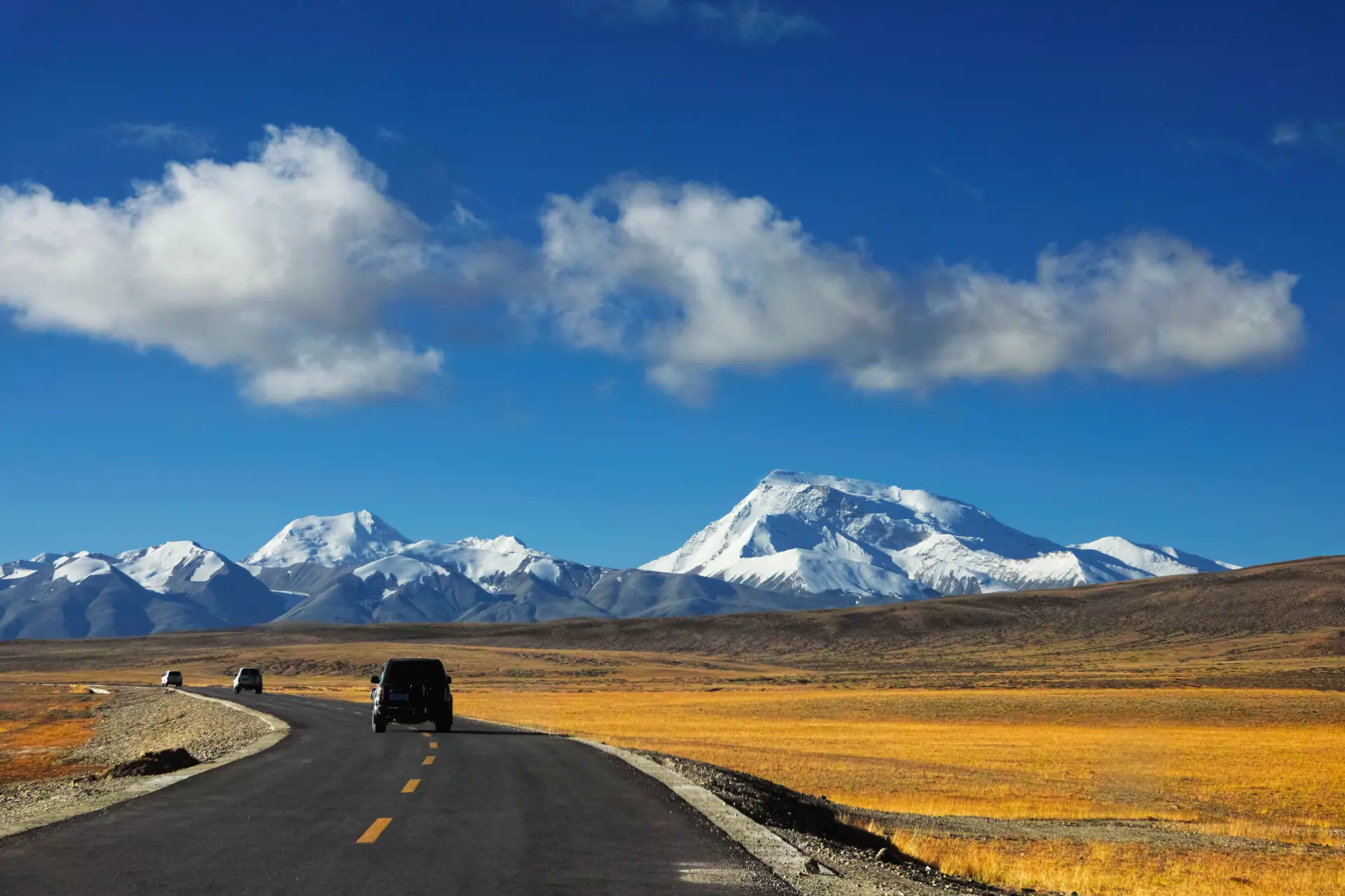 Open road across the Tibetan plateau toward snow peaks